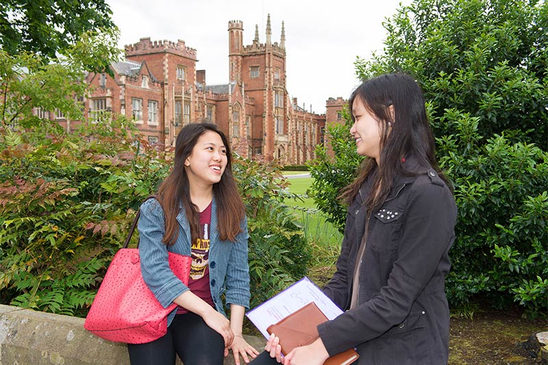 two female students chatting with lanyon building in the background