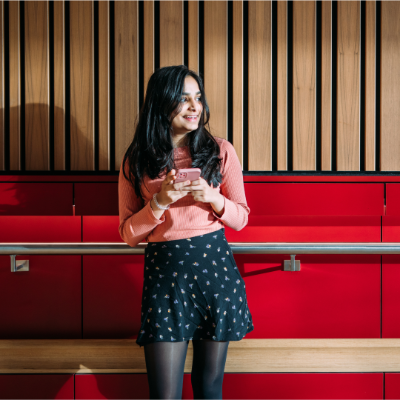 Female student standing by stairs holding phone looking away to her left