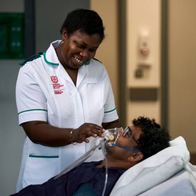 Female student nurse administering gas to a male lying down in a bed