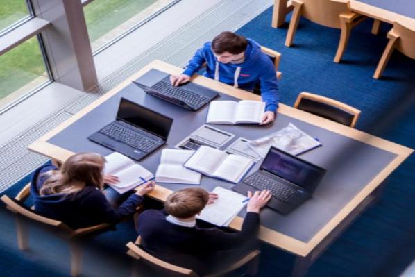 Overhead of 3 students studying with laptops and books in McClay Library