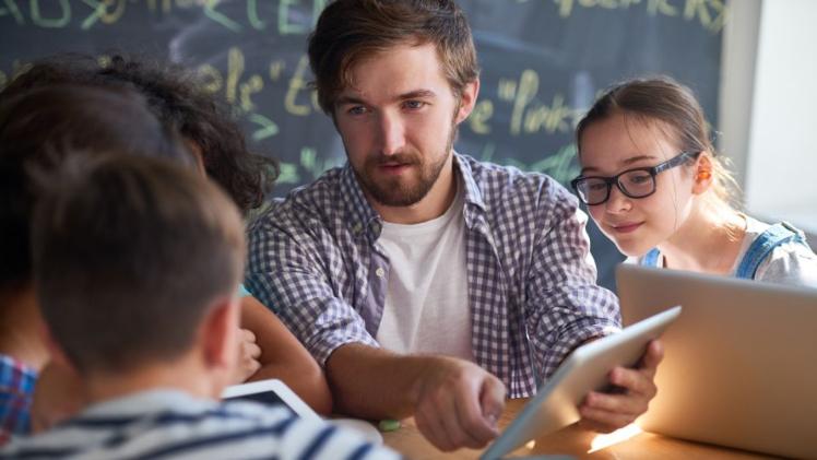 male teacher at a table with young primary school students