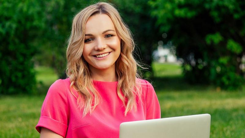 student sitting outdoors on laptop smiling to camera