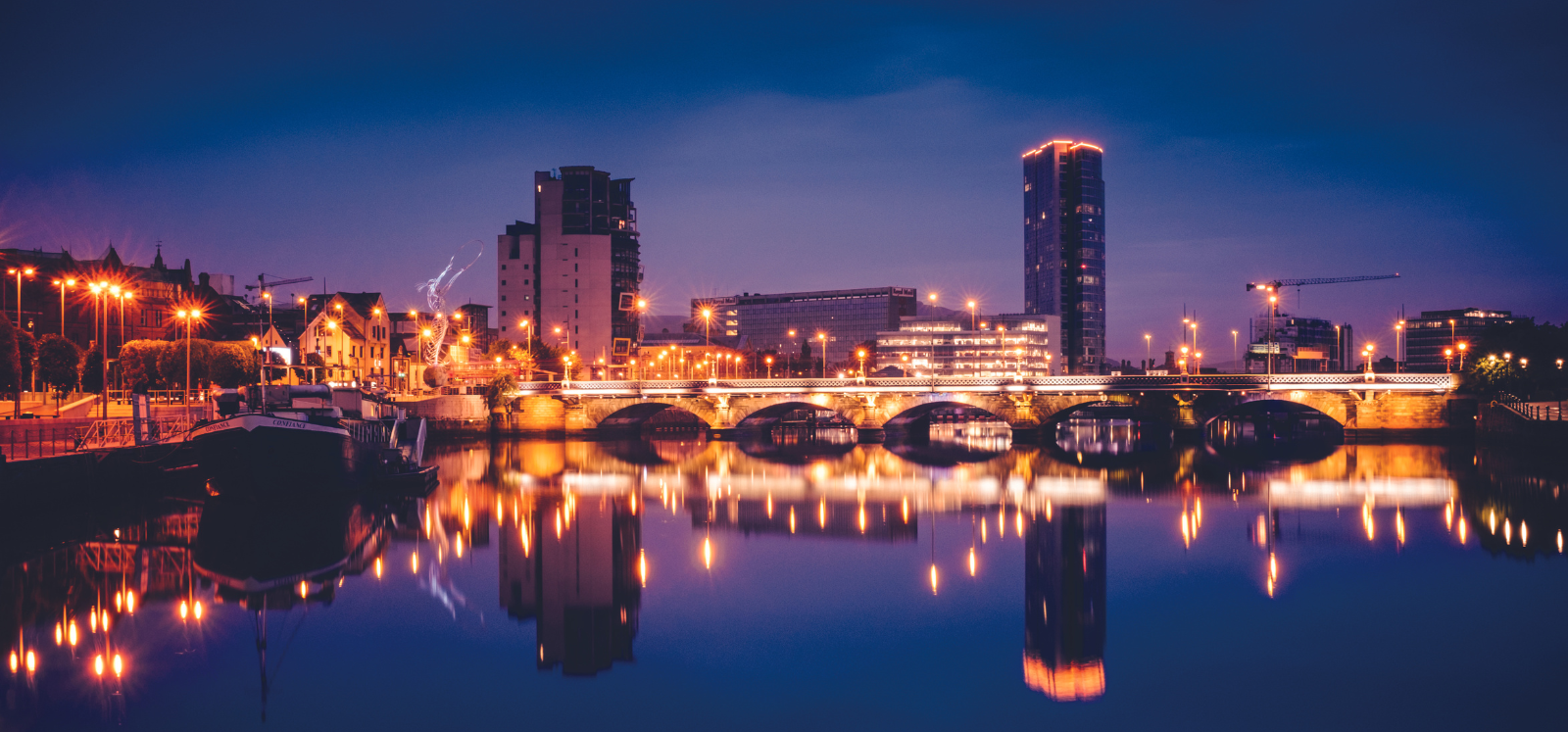 Image shows the river lagan lit up at night time, taken from City Quays