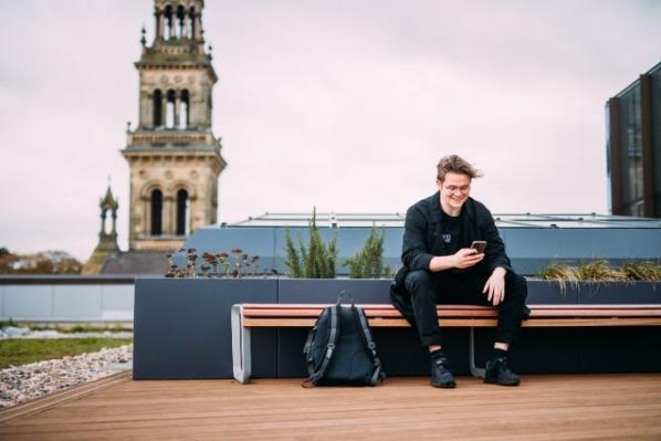 student sitting on rooftop of one elmwood looking at mobile across from lanyon building