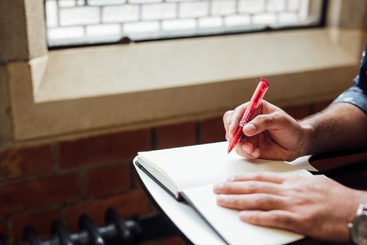 Student writing with a Queen's branded pen