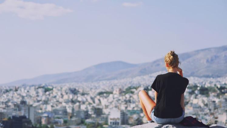 student sitting on a hilltop looking at a scenic view