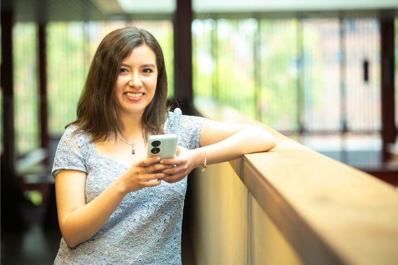 female standing with phone in hand smiling