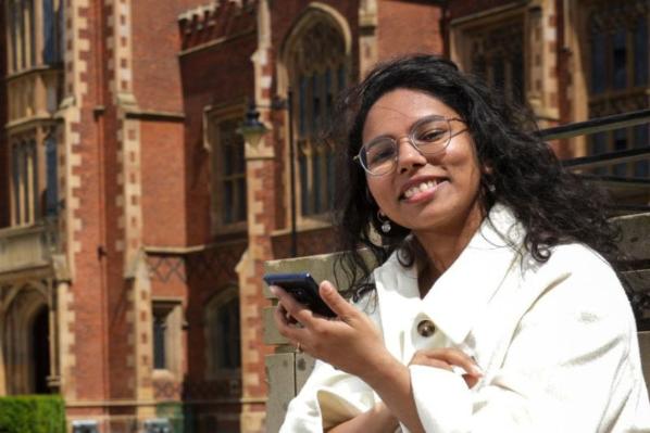 student sitting looking at phone in front of Queen's building