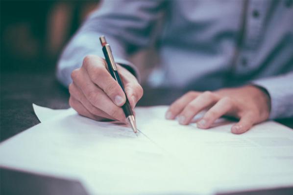 A person signs a document, whilst sat at a table.
