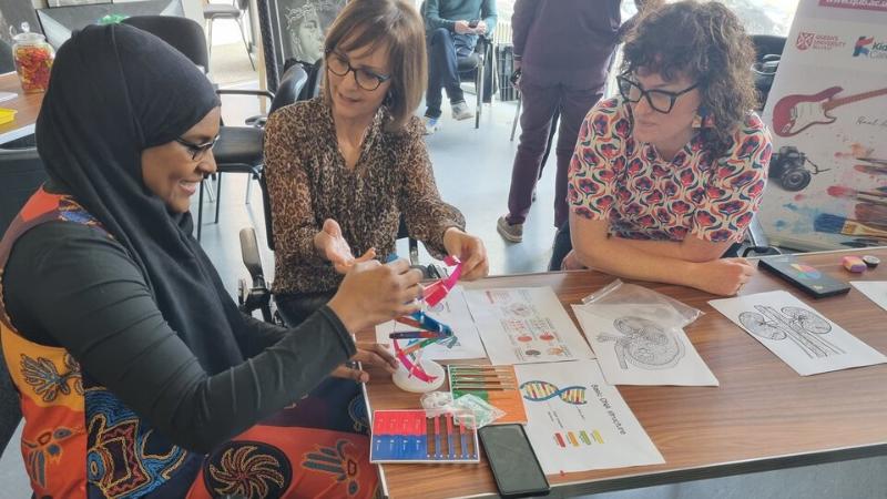 Woman learning about kidney dialysis from two women from the QUB Renal Arts Group