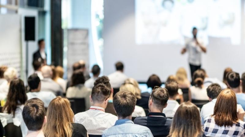 Group of people listening to a speaker on stage at a seminar