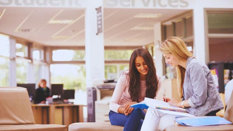 two females sitting chatting looking at a book