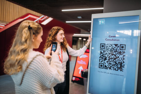 Two students scanning a QR code on a screen for career info