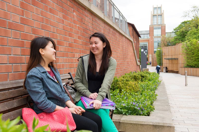 two international female students chatting on a bench outside the McClay library