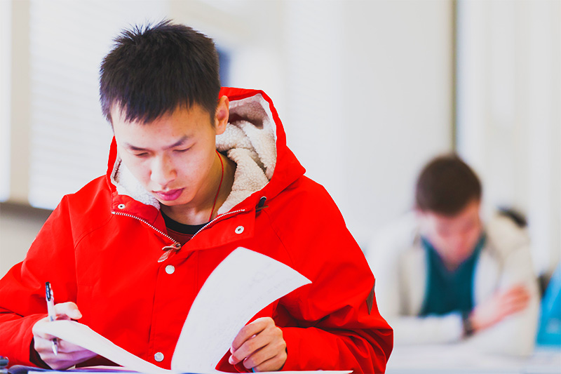 Student in red coat reading lecture notes