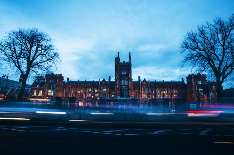 timelapse shot of Lanyon building at night time from across university road with cars in foreground