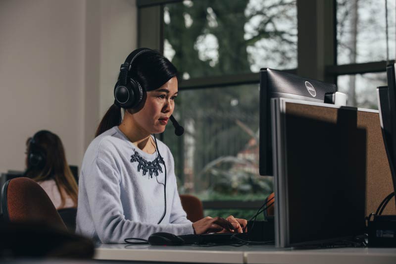 international student using a computer with headphones in the QUB language centre