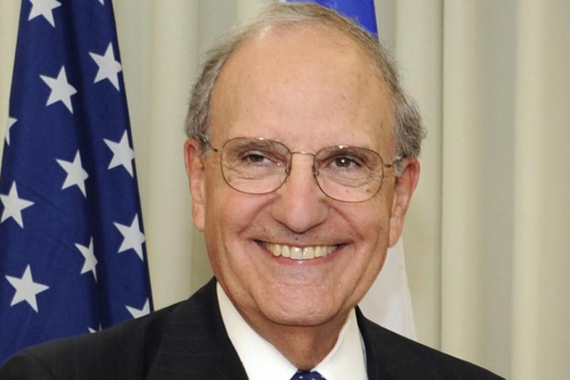 Senator George J. Mitchell smiling in front of the American flag