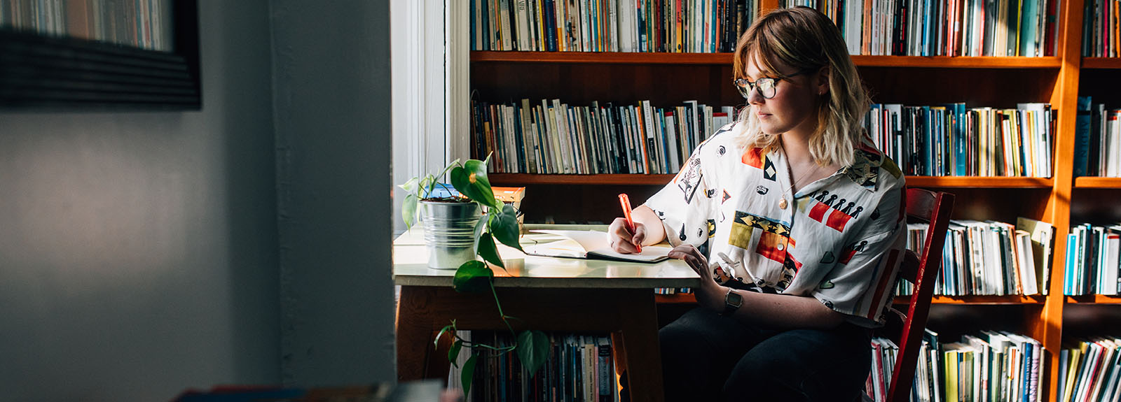 Student writing at desk with Bookshelf