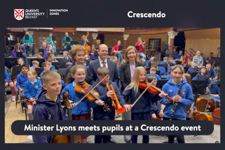 Minister Gordon Lyons with school pupils playing orchestral instruments in the Ulster Hall
