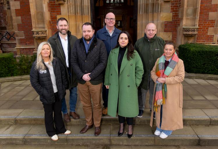 A group of people stand posed on the steps outside Queen's University Belfast looking towards the camera