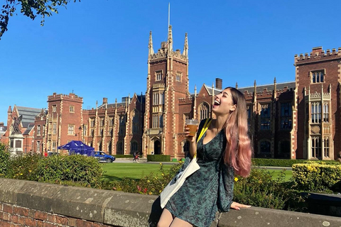 Student sitting on wall in front of Lanyon building laughing and holding an iced coffee