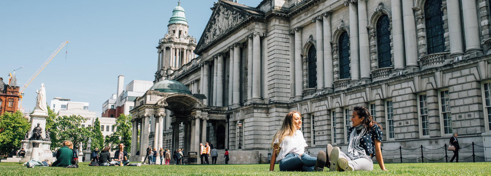 Two students sitting on grass outside the front of Belfast city hall