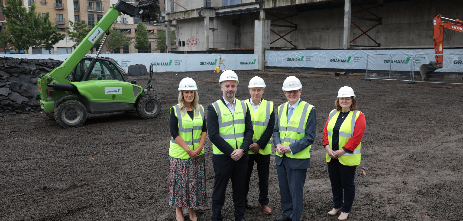 Five people in high-vis construction vests stand on a building site looking at the camera.