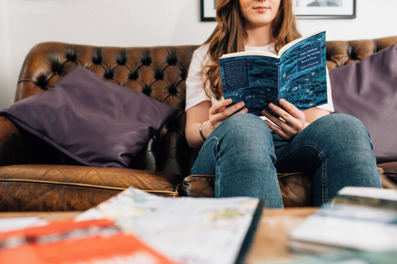 Female student reading book on sofa