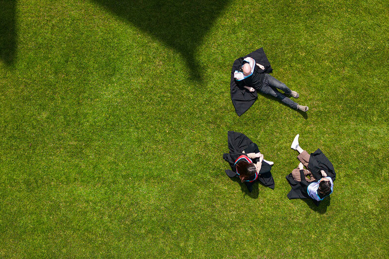 Three students in graduation robes sitting on grass lawn