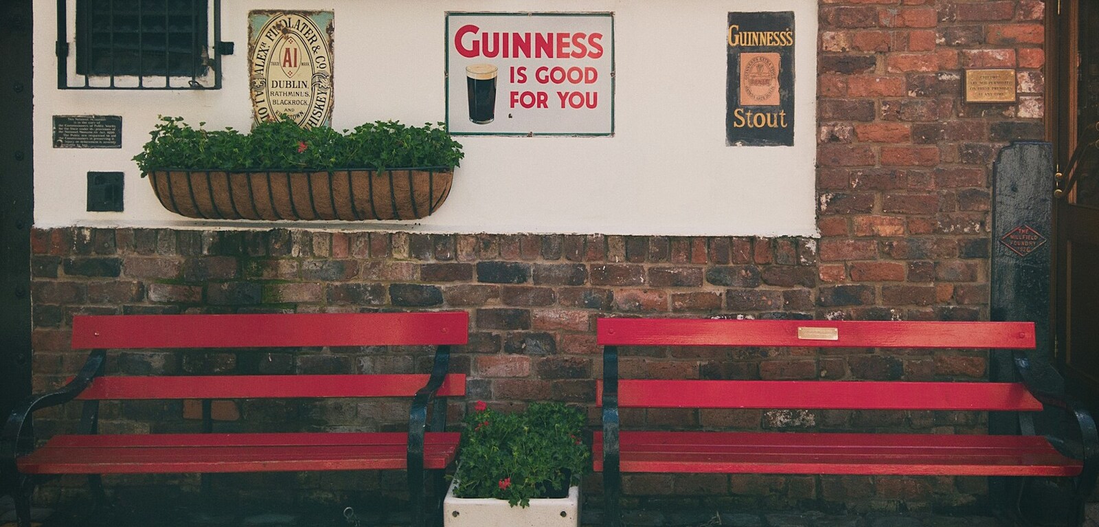 Red benches in front of a white wall with a Guinness sign