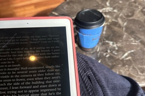 Student reading on kindle with Caffe Nero coffee on table beside her