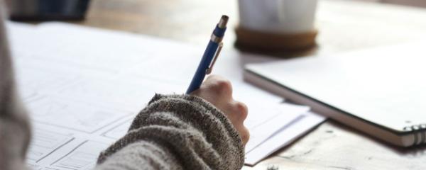 Person writing with a cup beside them