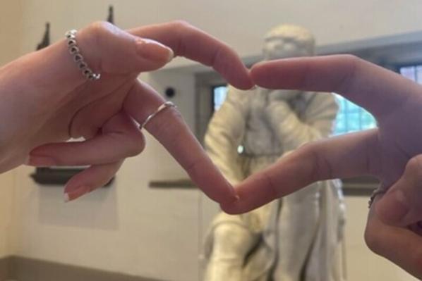 Student making heart sign with hands in front of Galileo statue