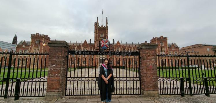 Student Sai Sree standing in front of the Lanyon gates in graduation robes