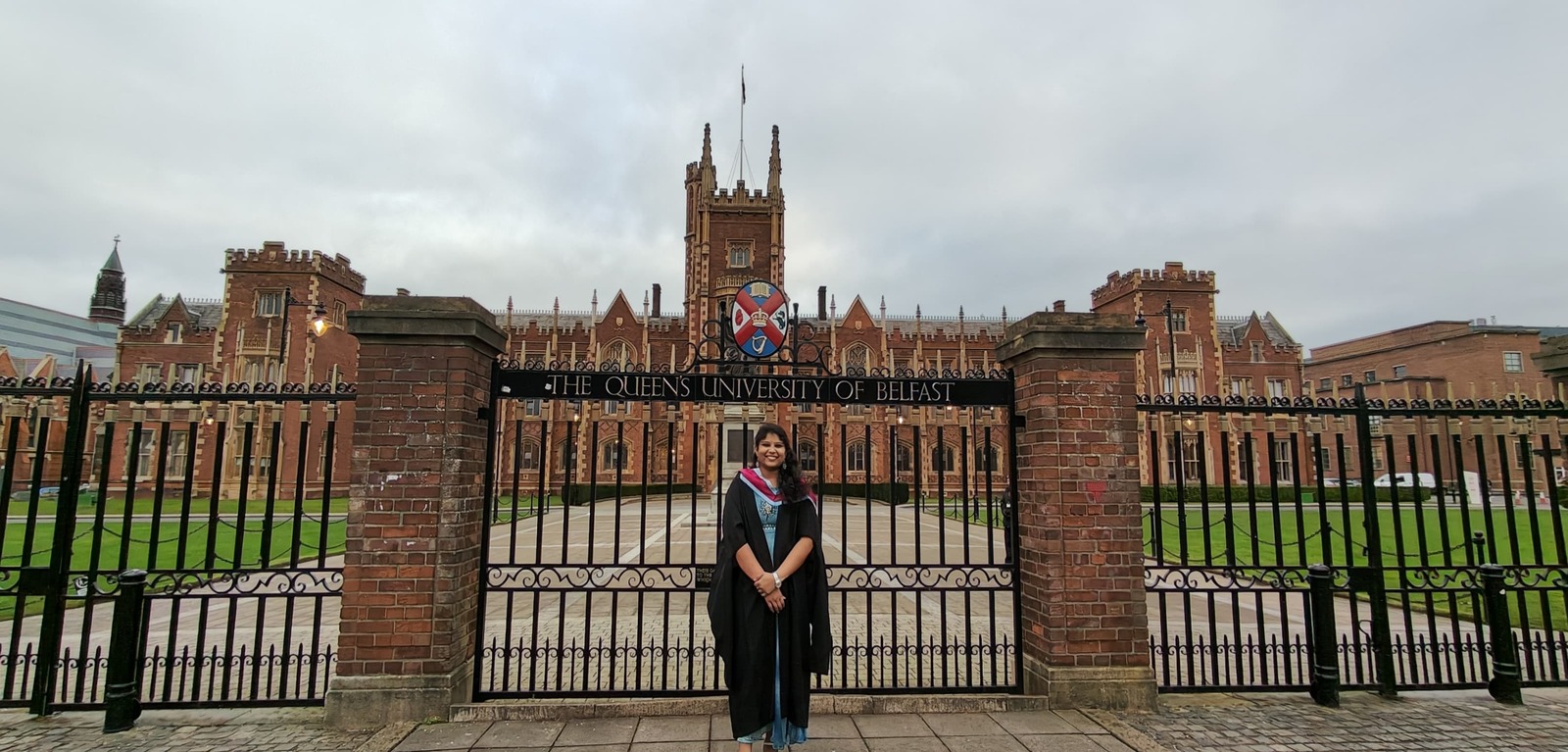 Student Sai Sree standing in front of the Lanyon gates in graduation robes