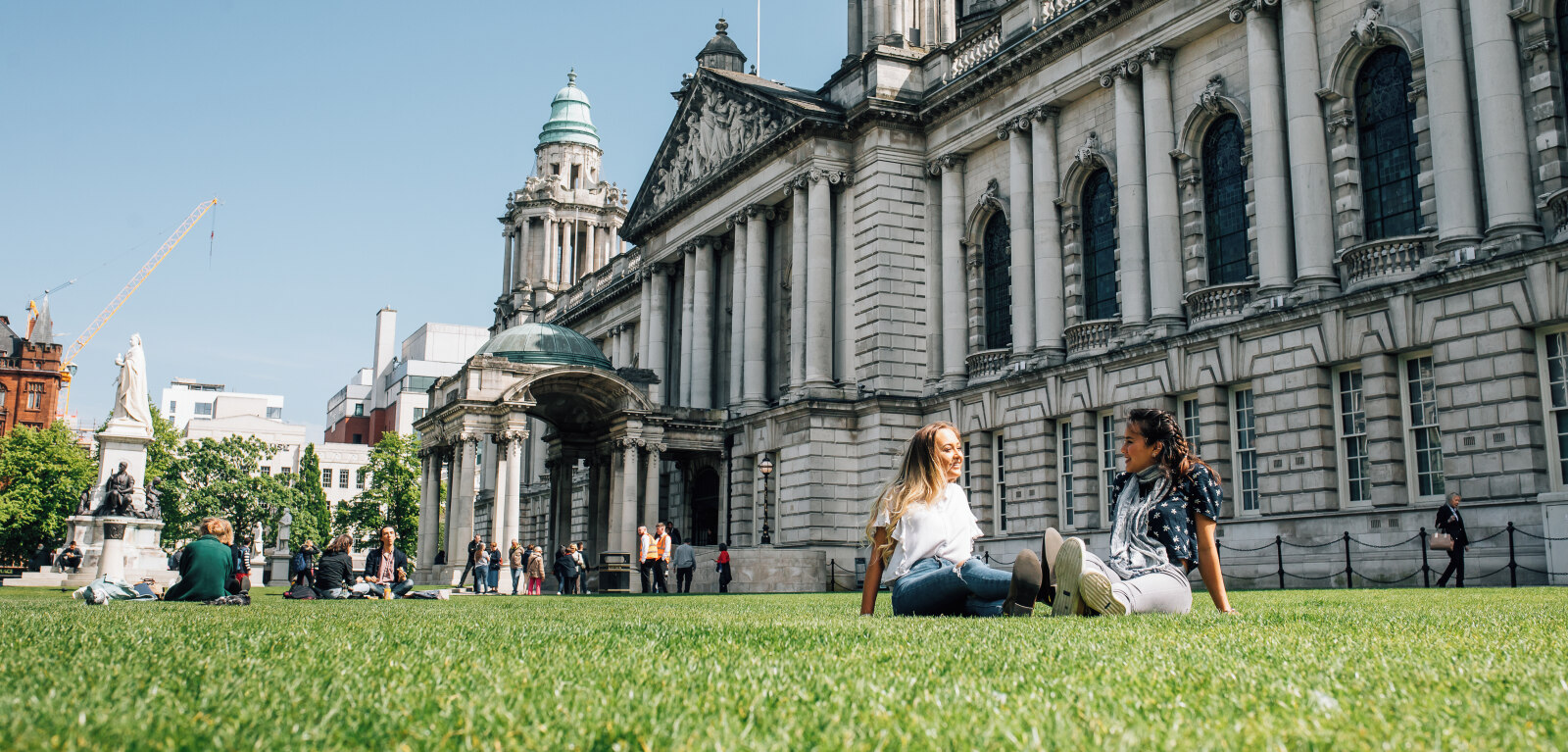 Two students sit on grass in front of City Hall