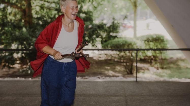 A person laughing as they run along holding drum sticks