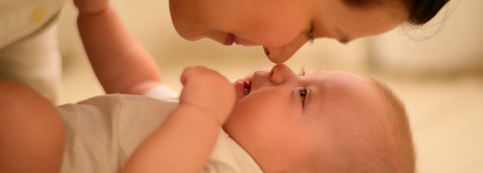 Baby lying on back with Mother leaning over to touch noses.