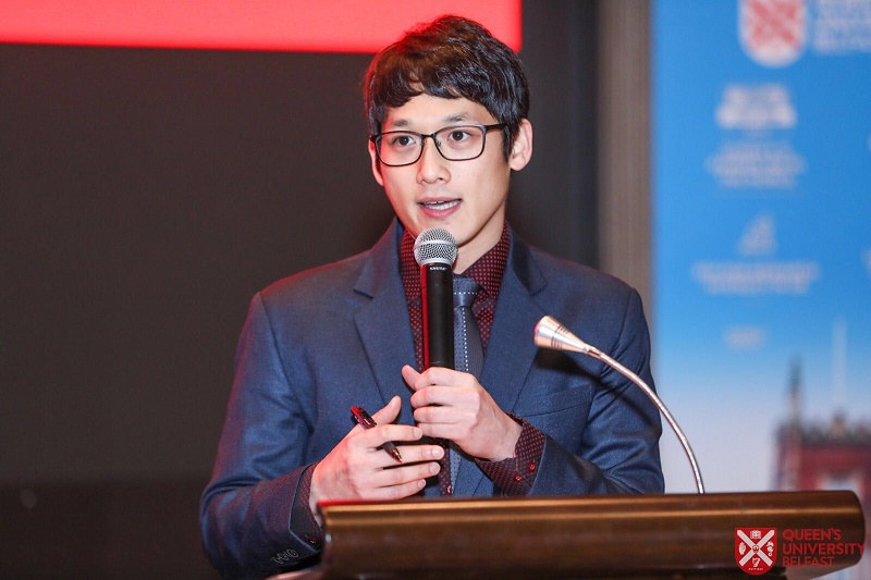 man standing at a lectern holding a microphone and speaking to an audience