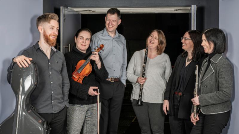 A group of six people in a doorway, four of them holding instruments.