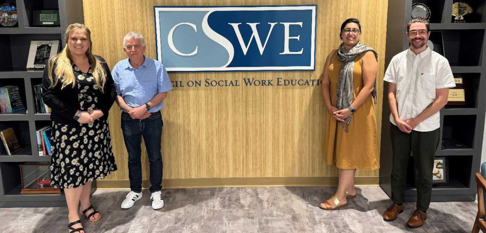 two men and two woman standing in front of a wood-panelled wall with the CSWE logo mounted on it