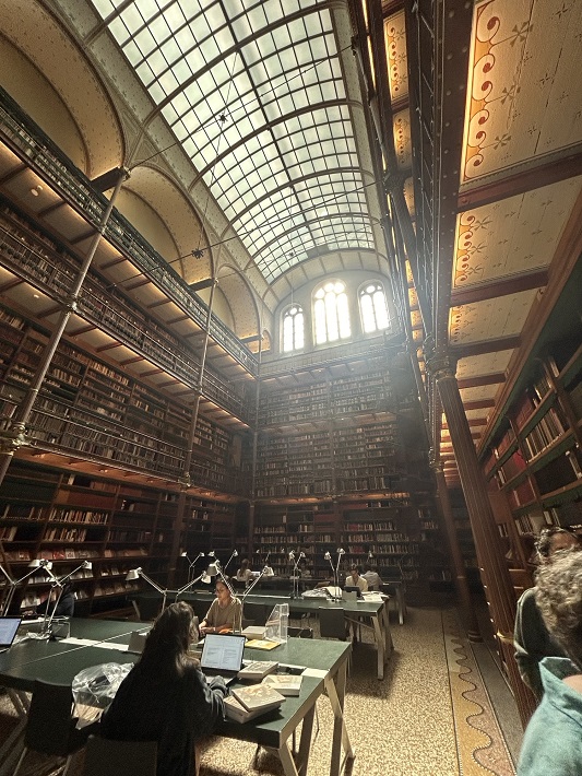 An old, high-ceiling, vaulted library with light streaming through arched windows. Young people are sat at desks studying below.