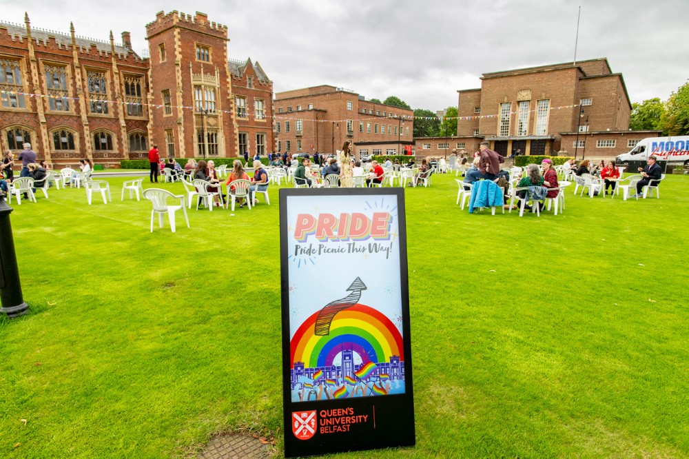 signage saying 'Pride Picnic this Way' on the lawn of Queen's Lanyon Building, showing seated picnic attendees in the background, July 2024